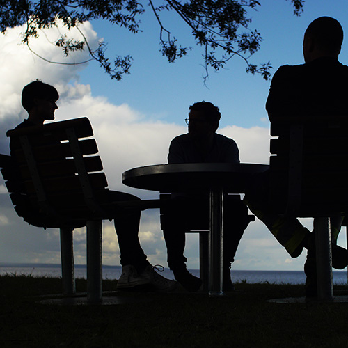 Prise de vue en contre-plongée de personnes assises sur des chaises de parc au crépuscule, leur silhouette se découpant sur le ciel du soir.